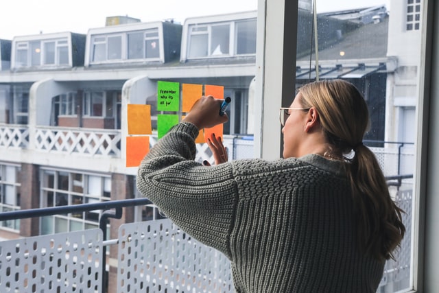 A woman writing on post-it notes stuck on the window of her apartment