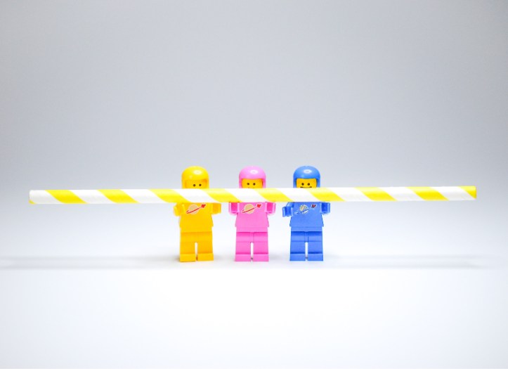Three Lego mini-figs of different colours work together to hold a straw. Image by Hello I'm Nik | unsplash.com