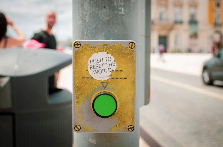 Green road-crossing button centred on image, with the label "Push to reset the world". Photo by Jose Antonio Gallego Vazquez  |  unsplash.com