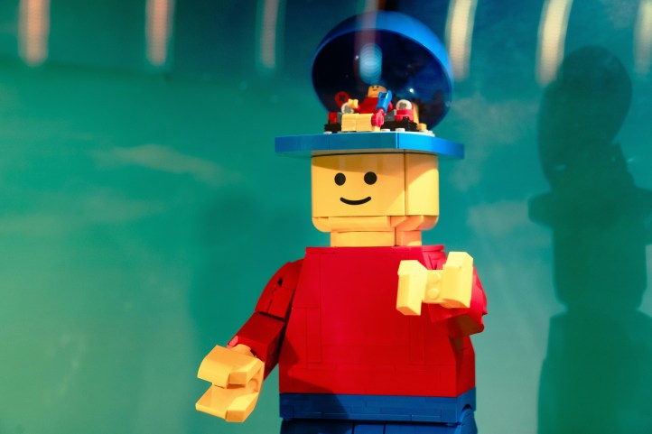 Lego minifig with red shirt and blue pants with an open head. Inside the open head is another mini-minifig , which is controlling the big minifig. 